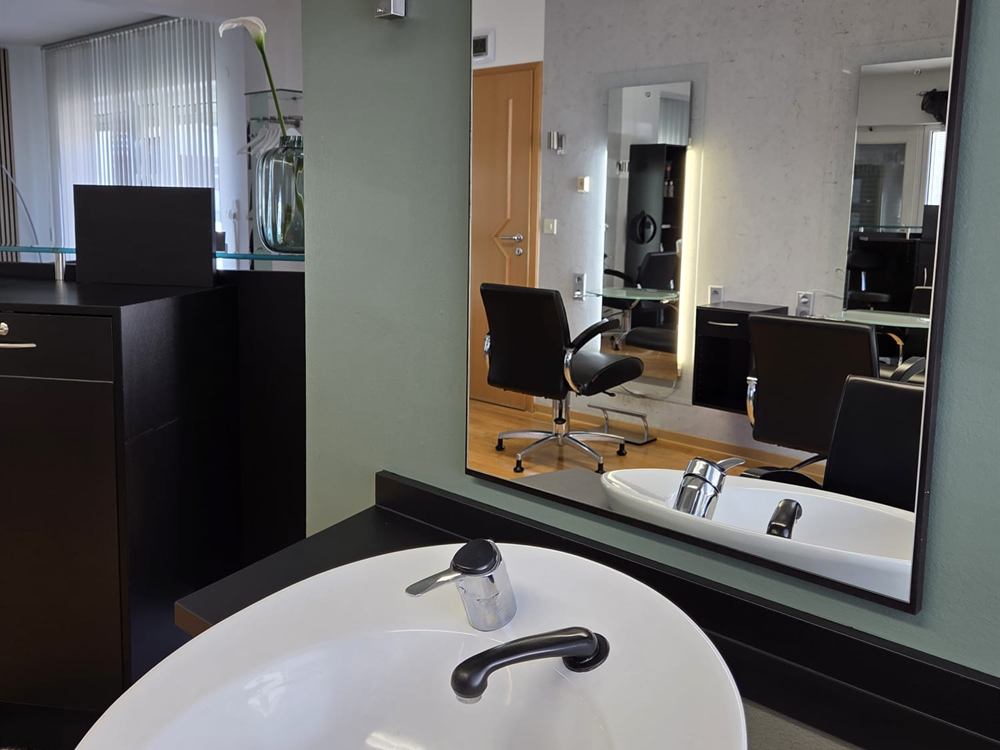 Waschbecken und beleuchteter Spiegel an einem Frisierplatz im Friseursalon Häfner