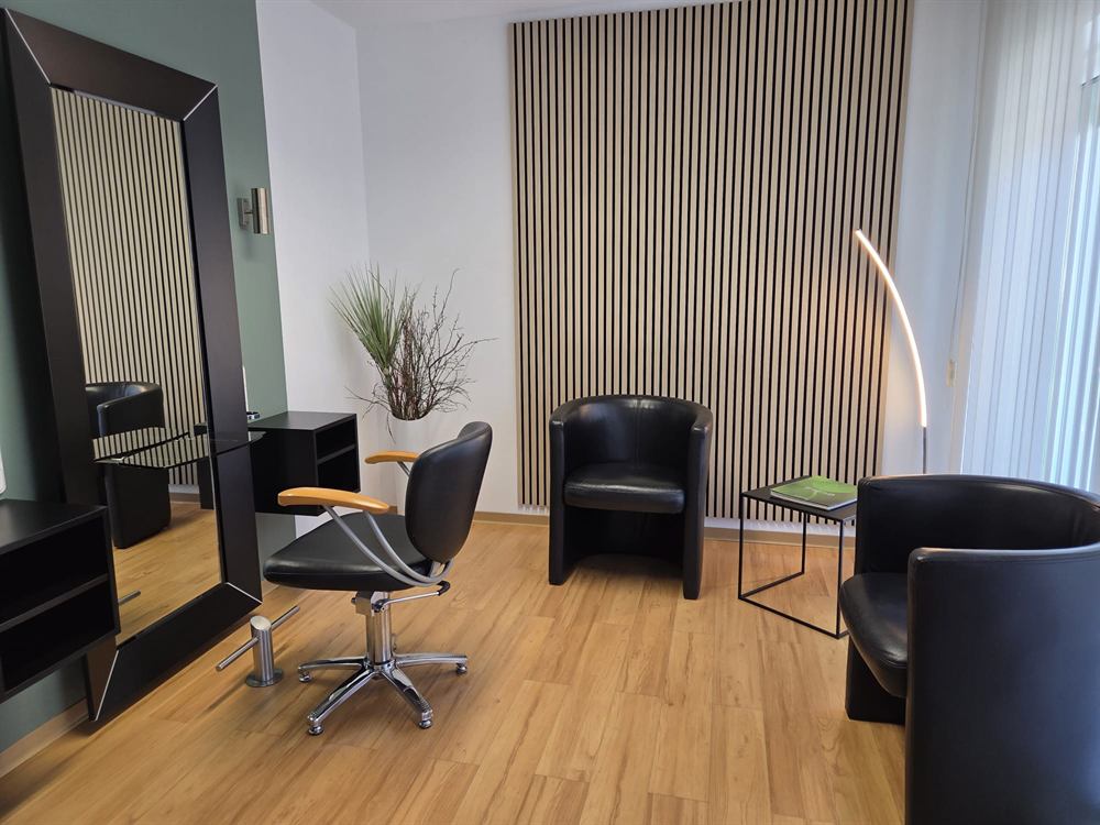 Wartebereich mit Sesseln vor einer Holzlamellenwand im Friseursalon Häfner
